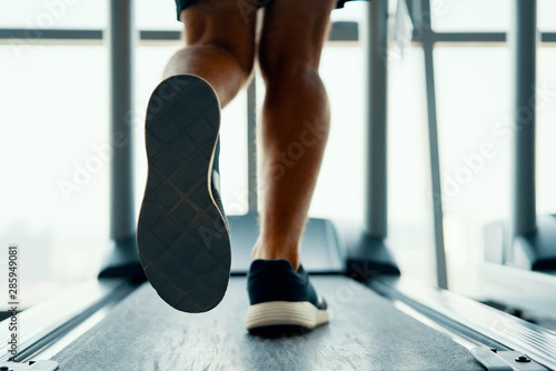 Close up male muscular feet in sneakers running on the treadmill at gym
