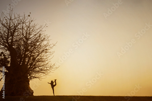 Young woman doing yoga exercise near a big tree