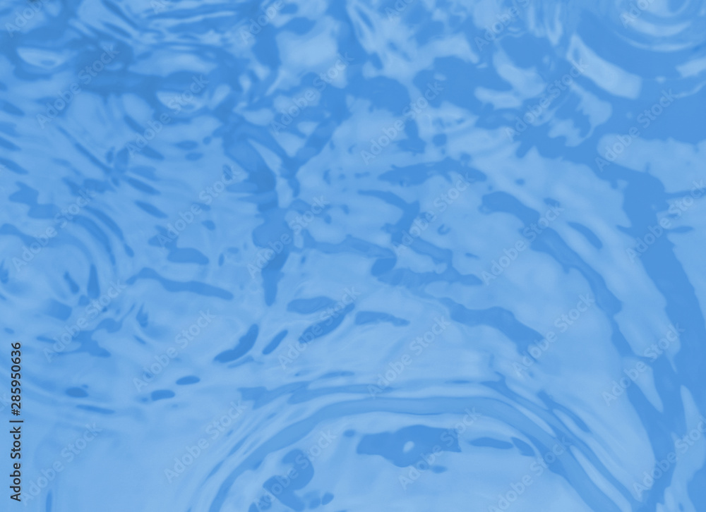 Concentric waves on blue water surface after falling drops, top view
