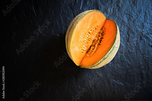 Small, cut melon lying on a stone slab. View from above.