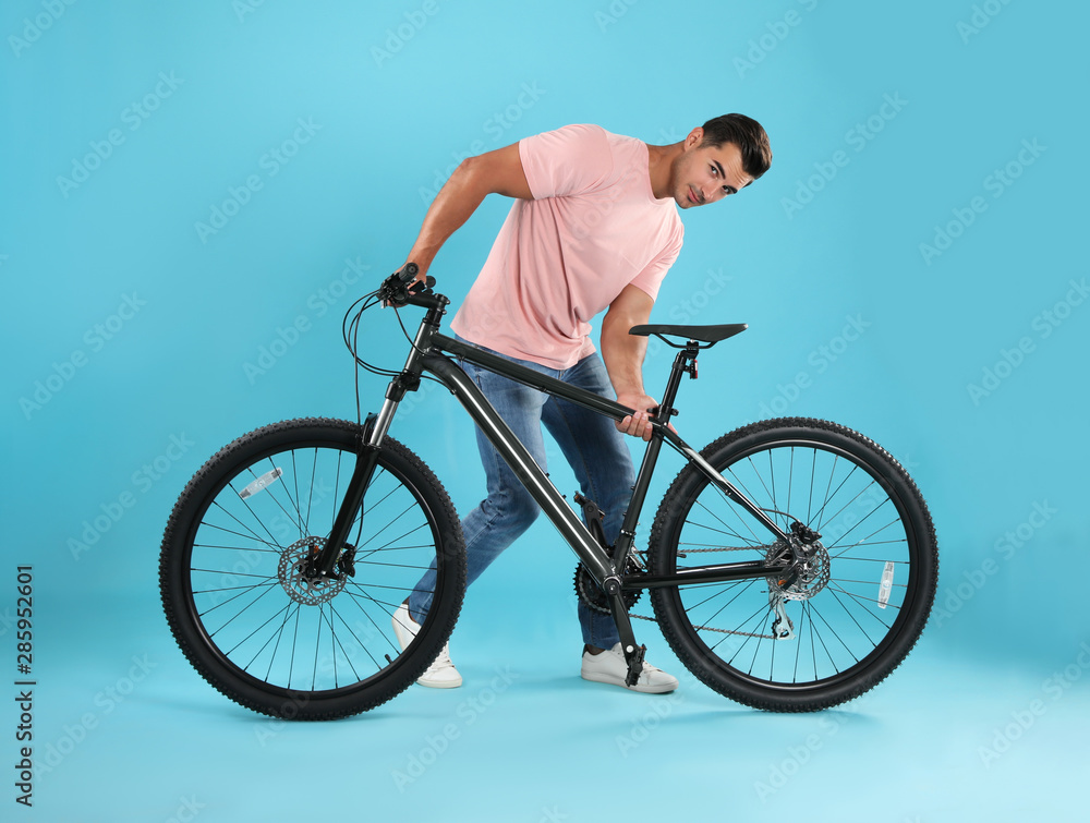 Naklejka premium Handsome young man with modern bicycle on light blue background