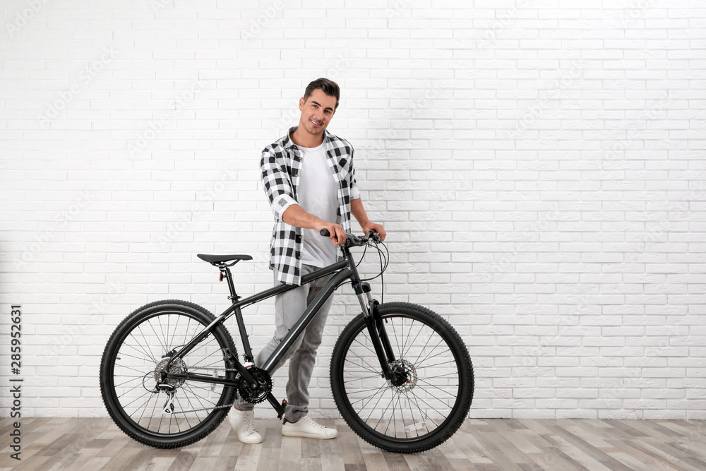 Handsome young man with modern bicycle near white brick wall indoors Handsome young man with modern bicycle near white brick wall indoors