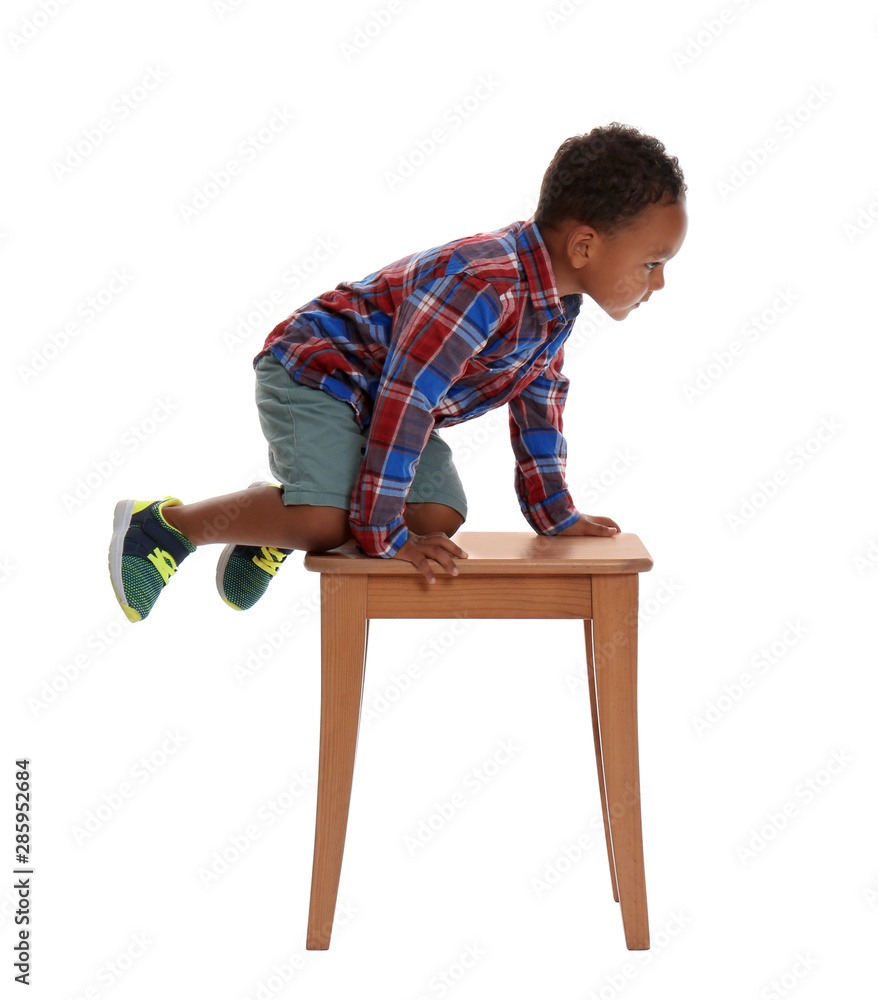 Little African-American boy climbing up stool on white background. Danger at home