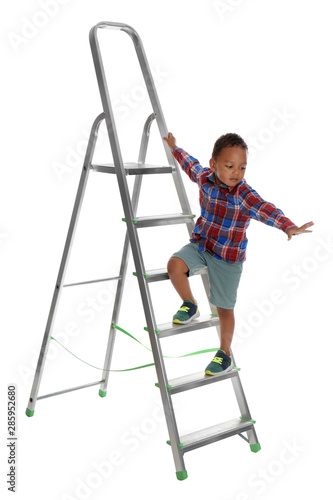 Little African-American boy climbing up ladder on white background. Danger at home