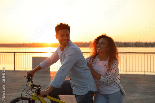 Young couple riding bicycle on city waterfront at sunset
