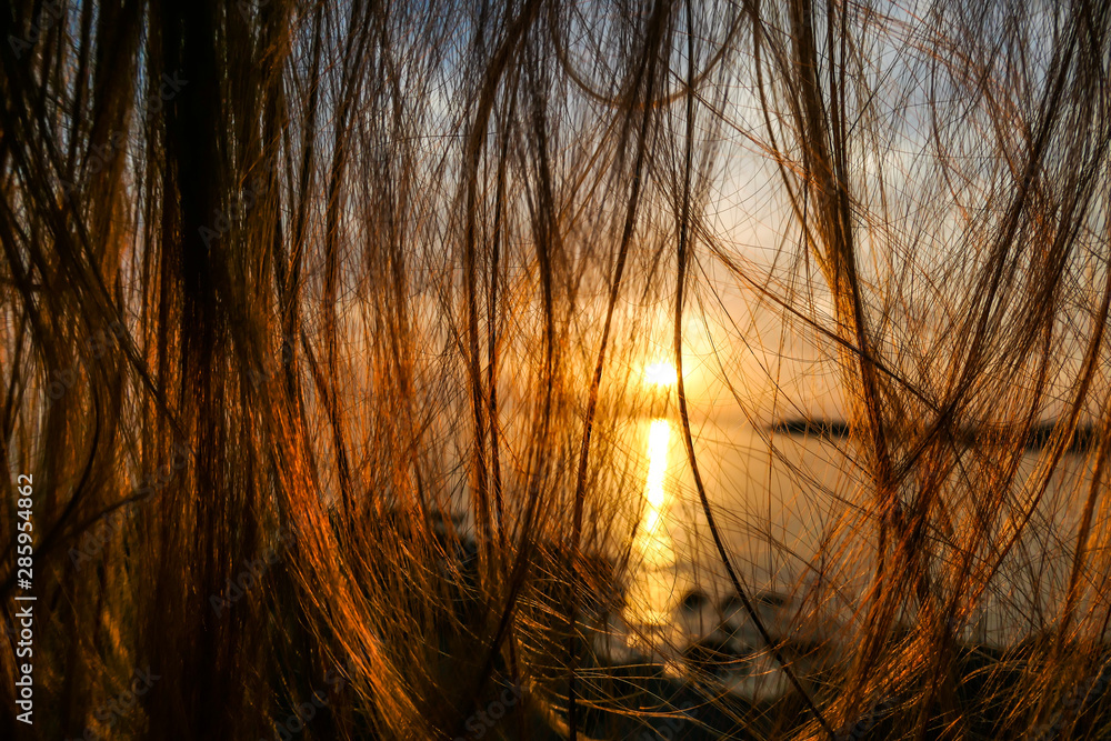 Long brunette hair hanging loose, disturbing the view on the setting sun by the beach. The sun sets over the horizon. The sun beams reflecting in the calm sea waters. There is an island on the side. Long brunette hair hanging loose, disturbing the view on the setting sun by the beach. The sun sets over the horizon. The sun beams reflecting in the calm sea waters. There is an island on the side.