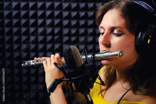 Girl flute player plays in music studio, copy space. Record wind musical instruments with a professional microphone. Woman in headphones flutist playing the western flute. photo