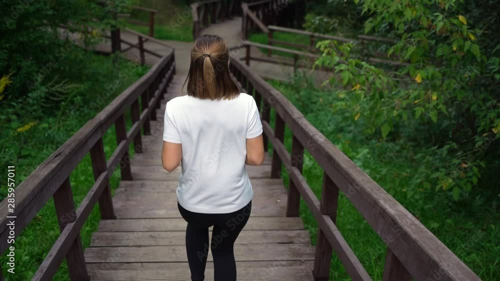 Slim fit girl running down the stairs in park. Young attractive fit girl or woman in white t-shirt and black sport pants Slim fit girl running down the stairs in park. Young attractive fit girl or woman in white t-shirt and black sport pants