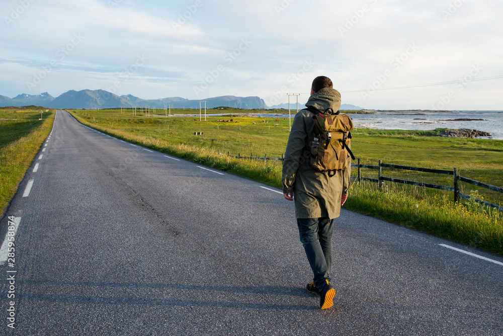 Man with backpack walking on an empty road. Amazing landscape, mountain and ocean. Scenic view. New way. Enjoy the moment, relaxation. Wanderlust. Travel, adventure, lifestyle. Explore North Norway Man with backpack walking on an empty road. Amazing landscape, mountain and ocean. Scenic view. New way. Enjoy the moment, relaxation. Wanderlust. Travel, adventure, lifestyle. Explore North Norway