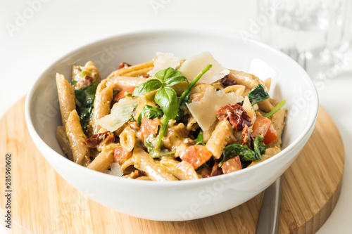 Whole wheat pasta with fresh and dried tomatoes, basil and parmesan cheese in white bowl