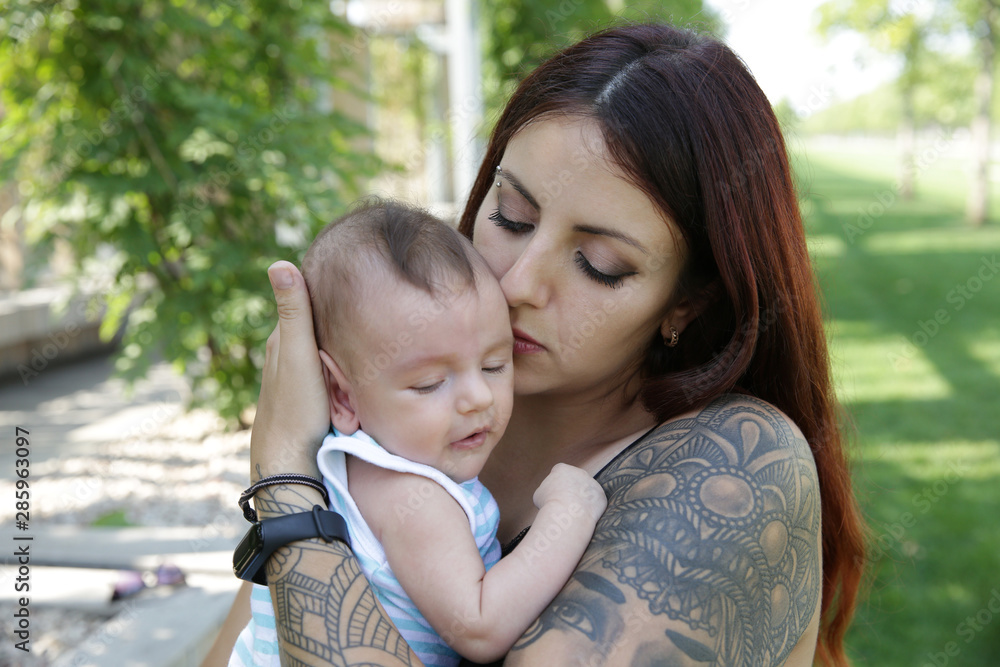 Portrait Happy young mother kisses her cute newborn baby. Happy family, motherhood, parenting, people and childcare concept. In the park. Portrait Happy young mother kisses her cute newborn baby. Happy family, motherhood, parenting, people and childcare concept. In the park.