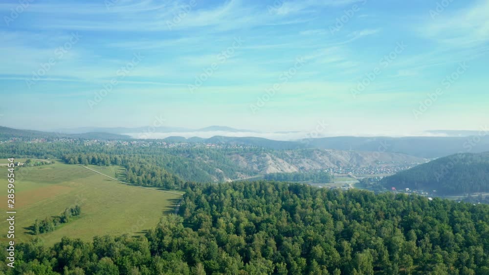 Beautiful landscape of mountain forest zone. View of the well-kept fields and the road nearby. In the distance there is a village. A small nebula over the valley on a sunny day. Beautiful landscape of mountain forest zone. View of the well-kept fields and the road nearby. In the distance there is a village. A small nebula over the valley on a sunny day.