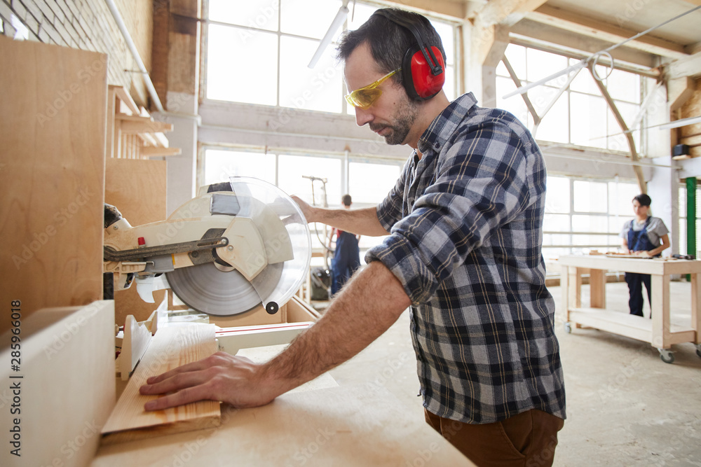 Side view portrait of mature carpenter sawing wood in industrial workshop, copy space Side view portrait of mature carpenter sawing wood in industrial workshop, copy space