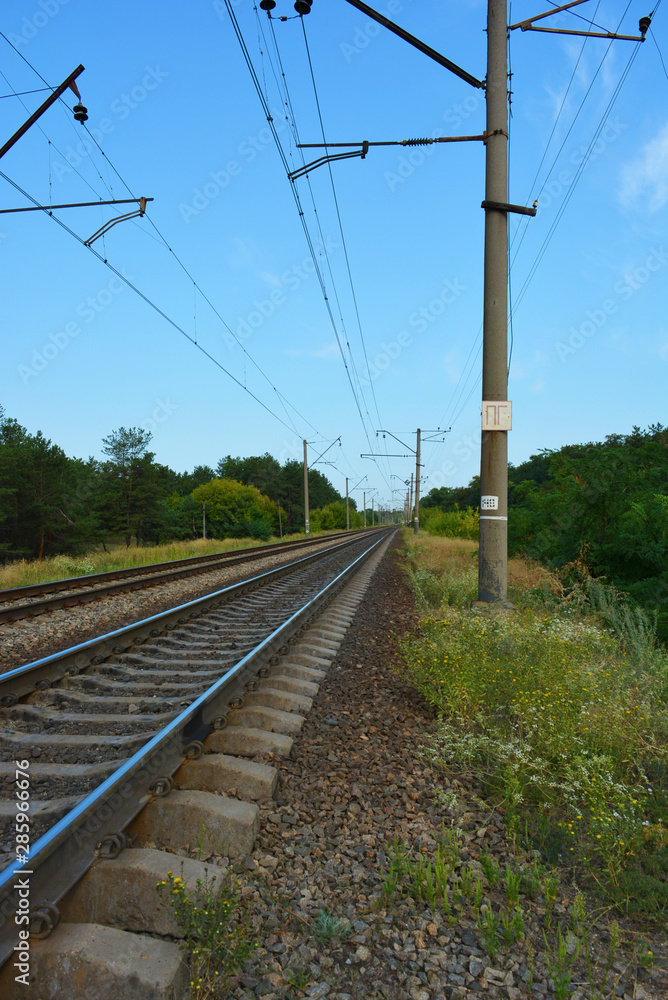 Railway track, railway and electric power lines for electric vehicles, electric trains lying along coniferous forests with blue sky, clouds. Infrastructure of Severny housing estate, Dnipro, Ukraine.