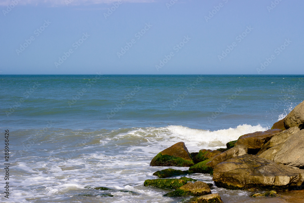 View on blue-turquoise sea water with white waves whitecaps on waves and sea foam against blue sky. Blue sea against sky. the sea against the sky. sea against sky and stones