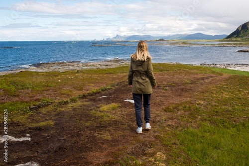 Blond hair girl walking, looks forward and enjoys a stunning scenic view. Ocean and rocks, beautiful landscape. Wanderlust. Adventure, freedom, lifestyle. Explore North Norway. Summer in Scandinavia