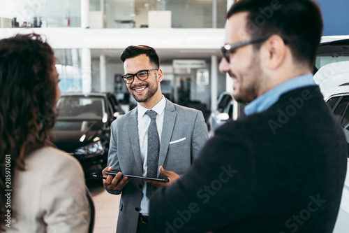 Middle age couple choosing and buying car at car showroom. Car salesman helps them to make right decision. photo