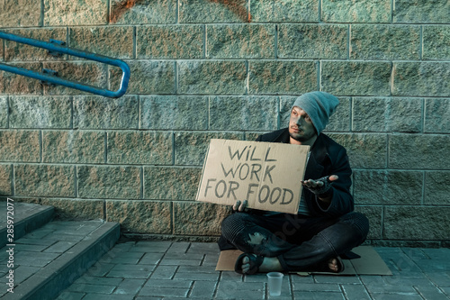 Foto A man, homeless, a man asks for alms on the street with a sign will work for food