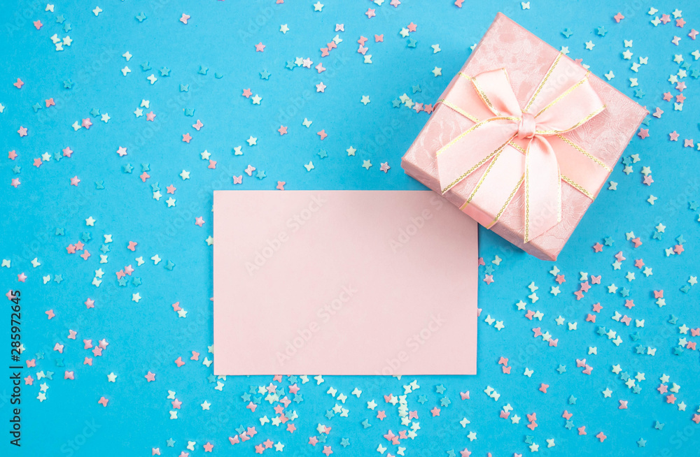 Layout for recording. Pink sheet for writing and gift box on a blue background with decorative multi-colored elements with stars and bows. Flat lay, top view Layout for recording. Pink sheet for writing and gift box on a blue background with decorative multi-colored elements with stars and bows. Flat lay, top view