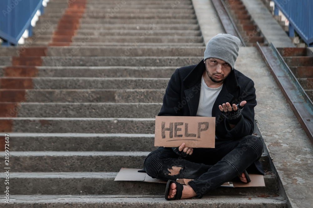 A man, homeless, a person asks for alms on the street with a Help sign. Concept of homeless person, addict, poverty, despair. A man, homeless, a person asks for alms on the street with a Help sign. Concept of homeless person, addict, poverty, despair.
