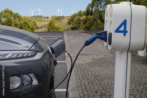 Carro eléctrico a carregar com paisagem de campo de energias eólica de fundo - energia renovável photo
