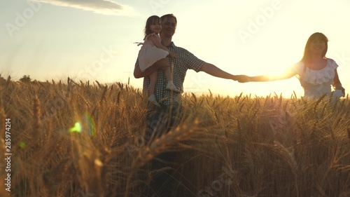 Happy young family with a child walks on a wheat field. father daughter and mother are playing on field. Mommy Mom and Dad are holding hands walking across a field of wheat. Slow motion.