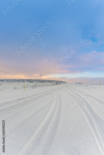 Tire tracks on snow covered road in an Arctic landscape under a cloudy evening sky above the Arctic Circle