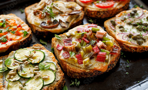 Vegetarian toast with grilled slices of bread with the addition of cheese and various vegetable toppings on a black background, close-up