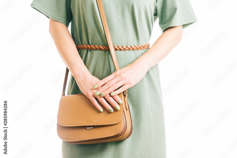 Woman in green dress standing with brown handbag.