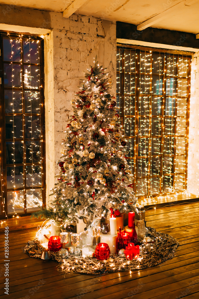 warm cozy magic evening in luxury old Christmas living room fairy tale interior design,pahoramic windows, Xmas tree decorated by lights,gifts, candles, lanterns, garland lighting.New year holidays