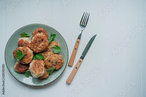 Cutlets with herbs served on a plate on a white wooden background.