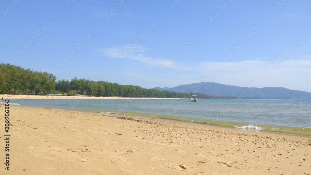 Tropical beach with small stones and sand near blue lagoon and boat with people are playing and swimming in background Tropical beach with small stones and sand near blue lagoon and boat with people are playing and swimming in background