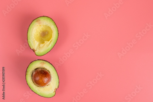 Two halves of avocado with stone on pink background. 