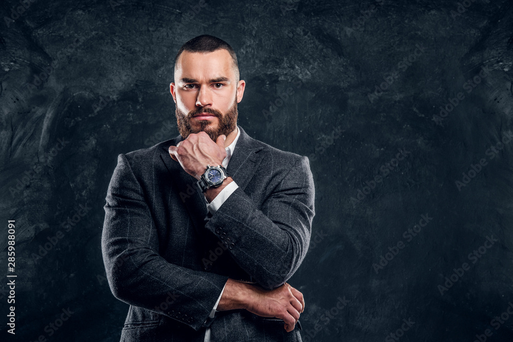 Sceptical bearded man in suit and white shirt is posing for photographer at dark studio. Sceptical bearded man in suit and white shirt is posing for photographer at dark studio.