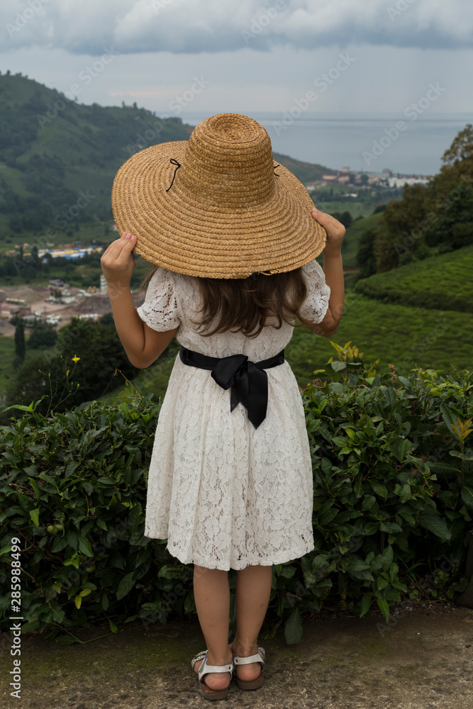 a beautiful girl wearing dress and wicker hat looking at the green tea field landscape with sea in the village from Rize Turkey.