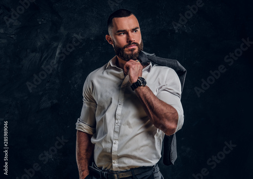 Pensive bearded businessman in white shirt is posing for photographer over dark background.