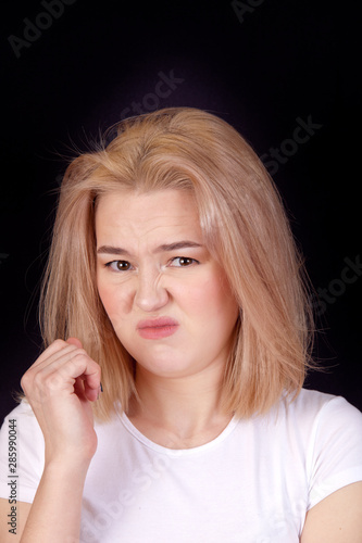 Portrait of a young blonde woman in a white T-shirt on a black background looking contemptuously and appreciatively. Concept emotion appreciation and contempt