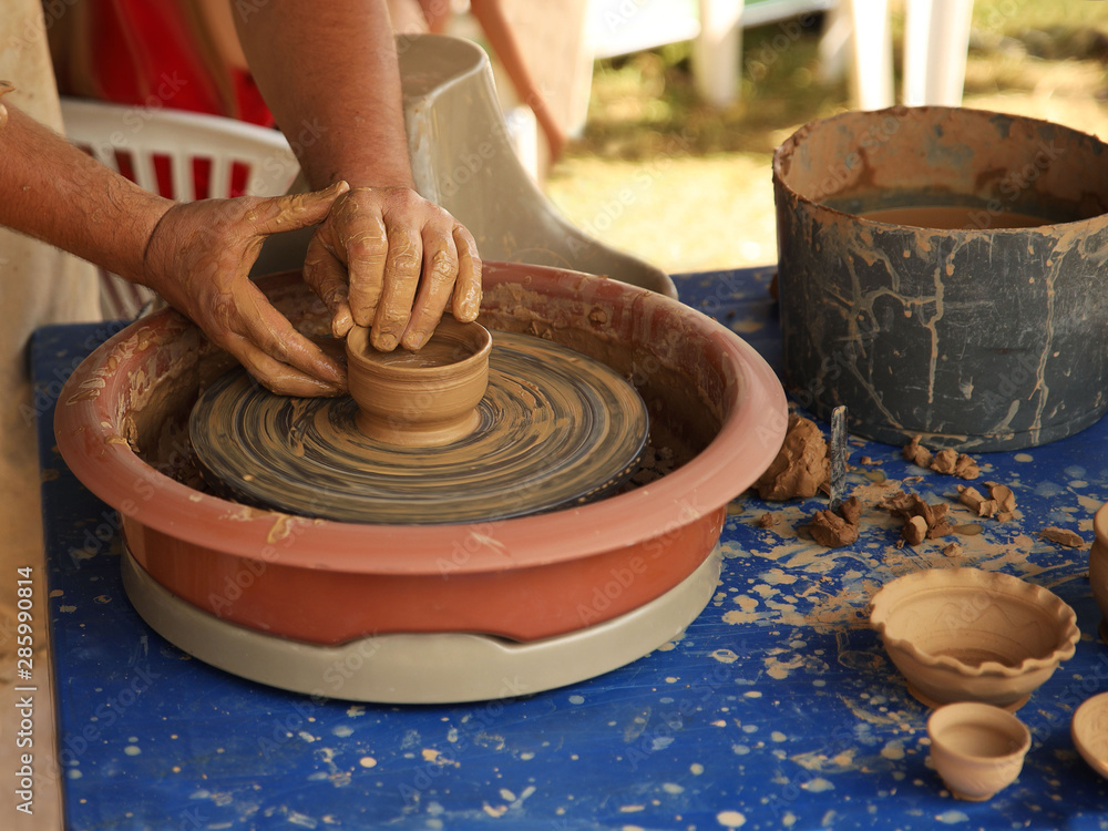 Hands of a potter sculpt clay dishes on a pottery wheel. Folk craft for  making dishes.