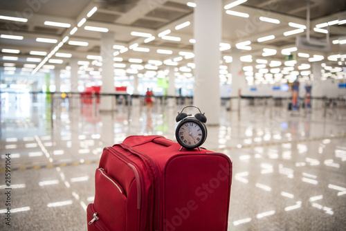 Time to travel or travel delay concept. Black Alarm clock on red suitcase. Abstract photo.
