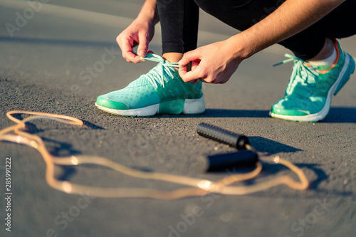 Fitness woman is tying shoelaces on sneakers and is preparing to do cardio exercises with skipping rope outdoors