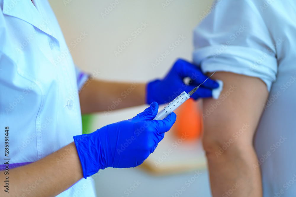 Nurse in gloves making a vaccination in the shoulder patient in hospital room. Flu shot, protection and prevention of viral infectious diseases Nurse in gloves making a vaccination in the shoulder patient in hospital room. Flu shot, protection and prevention of viral infectious diseases