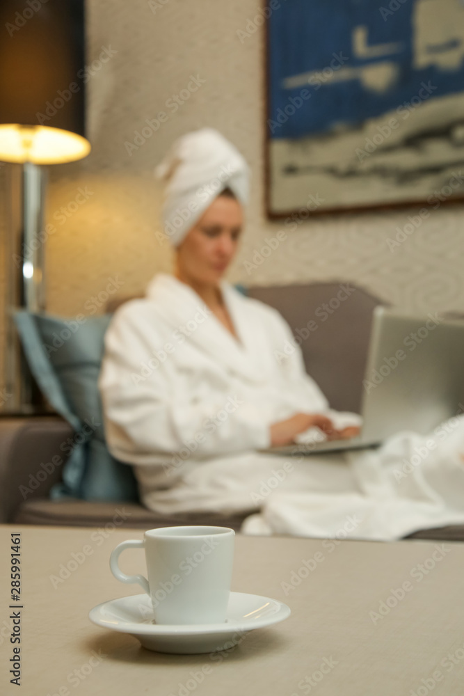 Woman in a white bathrobe working on the laptop, relaxing after a long day, spending a cozy evening alone Woman in a white bathrobe working on the laptop, relaxing after a long day, spending a cozy evening alone