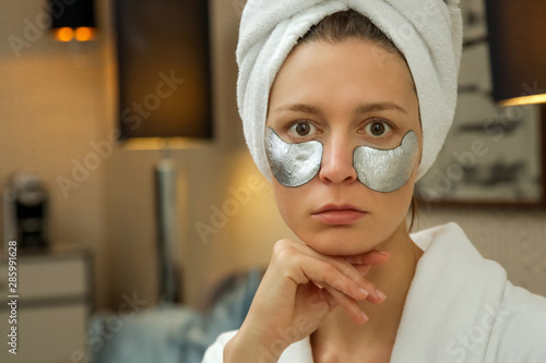 Woman in bath robe and wrpped head towel with under-eye patch mask for soothing, brightening and renewing. Reduces puffiness, dark circles and fine lines. Intense moisture treatment for the delicate u