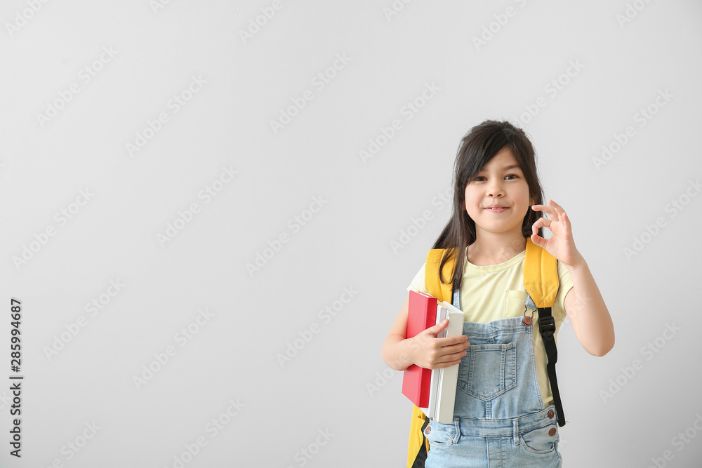Portrait of little schoolgirl showing OK gesture on light background Portrait of little schoolgirl showing OK gesture on light background