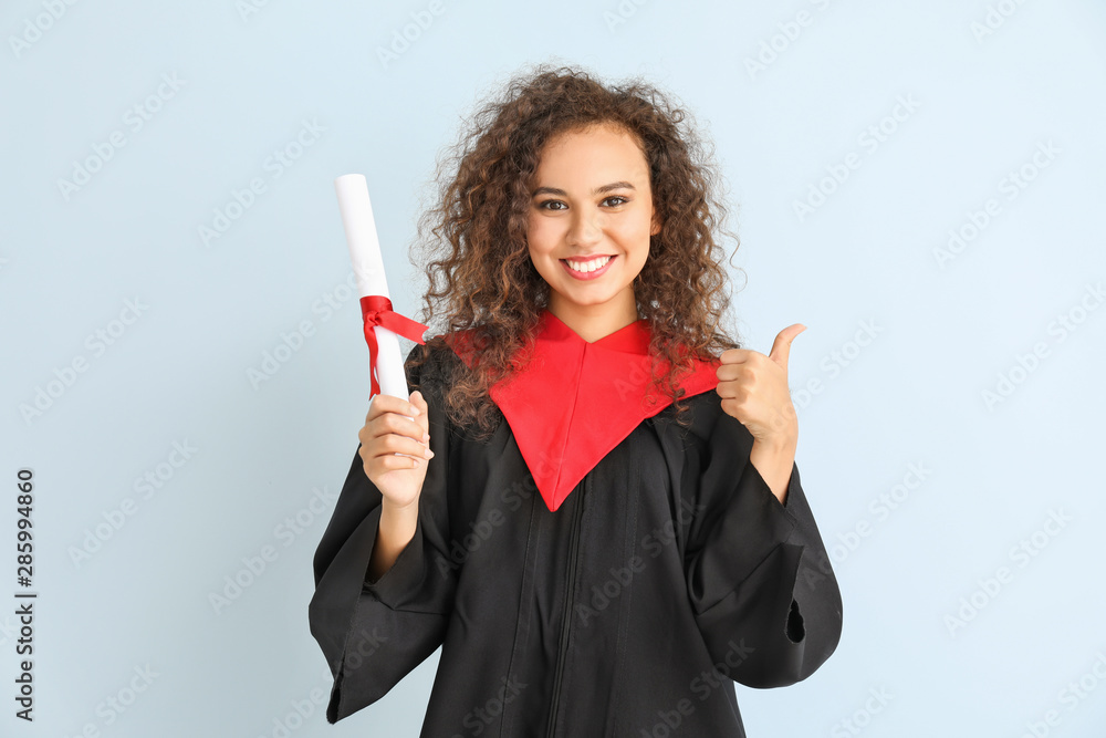 Young African-American student in bachelor robe showing thumb-up on color background Young African-American student in bachelor robe showing thumb-up on color background