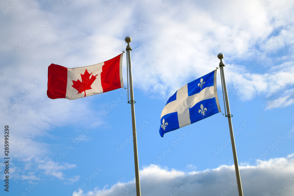 Fototapeta premium Flagi prowincji Quebec i Kanada łopoczące razem na wietrze na błękitnym niebie