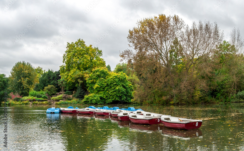 Panoramic view of a boating lake with paddle boats parked and park cafe outdoor tables, Battersea Park, London Panoramic view of a boating lake with paddle boats parked and park cafe outdoor tables, Battersea Park, London