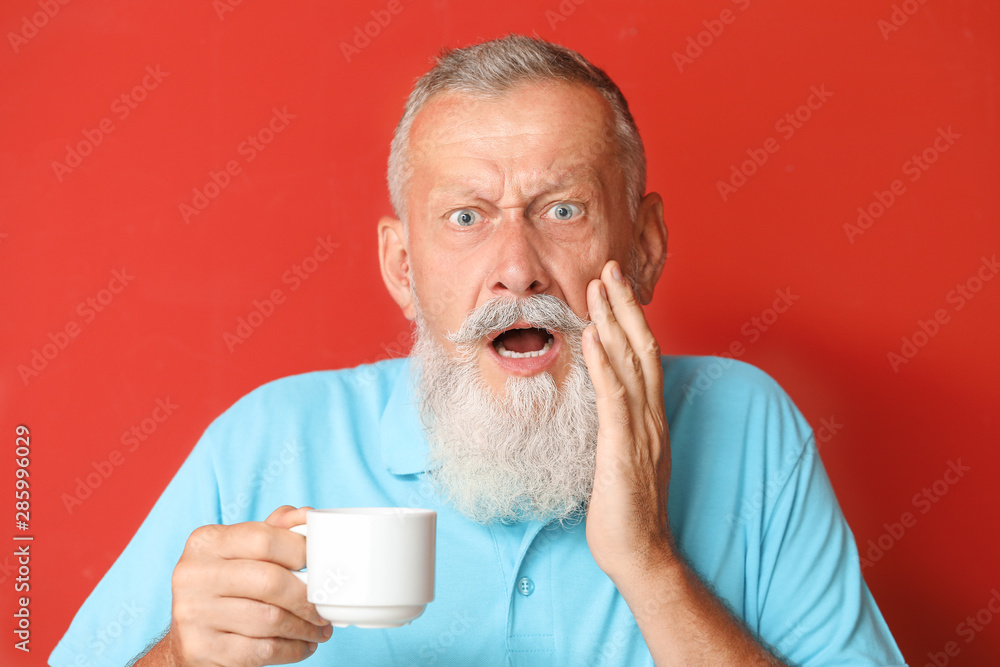 Senior man with sensitive teeth and cup of hot coffee on color background Senior man with sensitive teeth and cup of hot coffee on color background