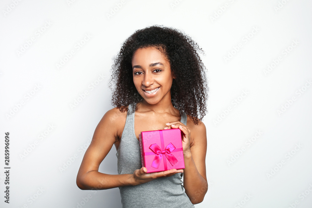 Portrait of beautiful African-American woman with gift box on white background