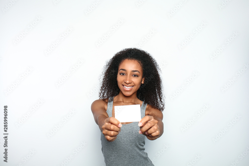 Portrait of beautiful African-American woman with blank business card on light background Portrait of beautiful African-American woman with blank business card on light background